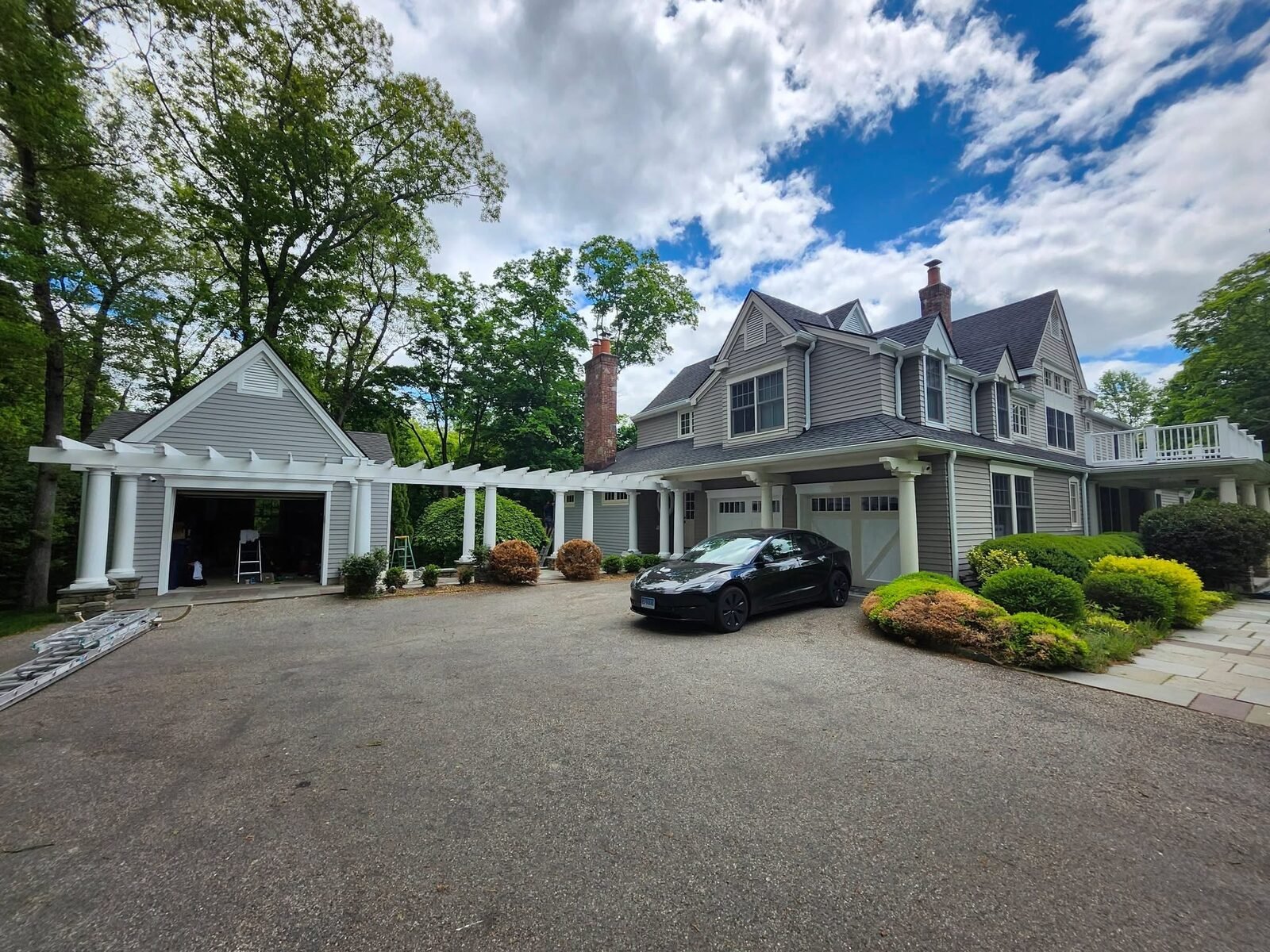 Freshly painted gray shingle home with white pergola and columns