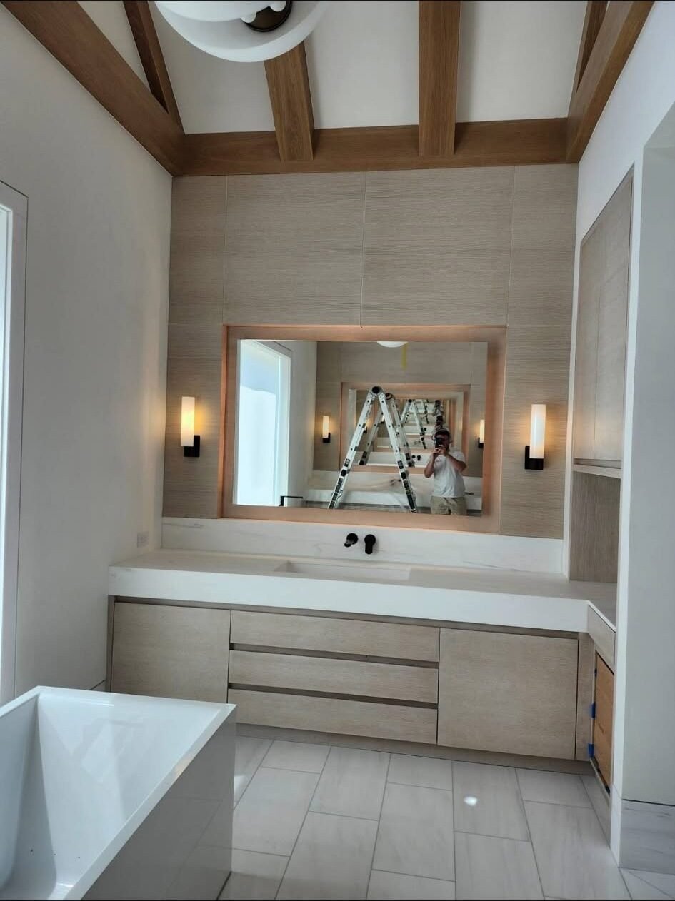 Painter reflected in the mirror of a freshly finished spa-style bathroom with wood beams
